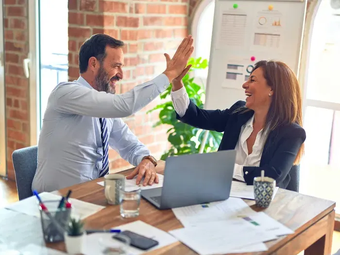 Two business professionals smiling and giving a high five during a successful meeting in a bright office